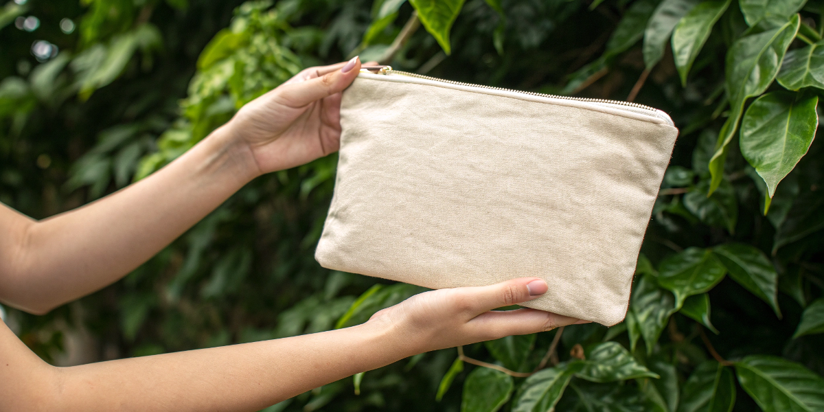 Sustainability of Bag Materials An organic cotton cosmetic bag held in hands with a green, leafy background