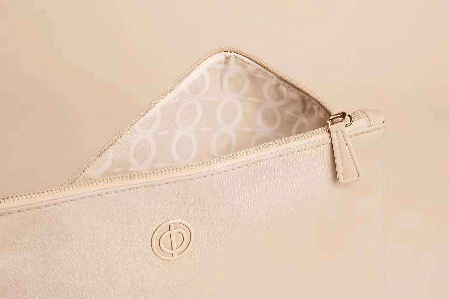 A close-up of a custom makeup bag showing a debossed logo, a custom zipper pull, and a patterned interior lining